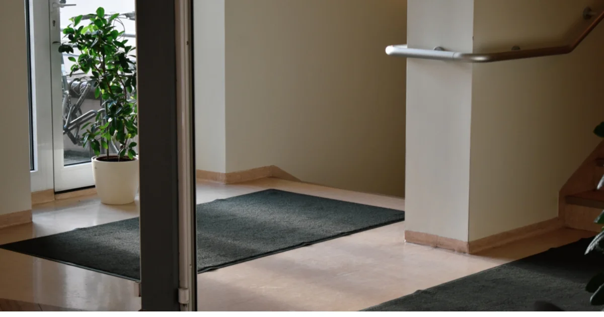 Indoor entryway with multiple dark floor mats arranged near a staircase.